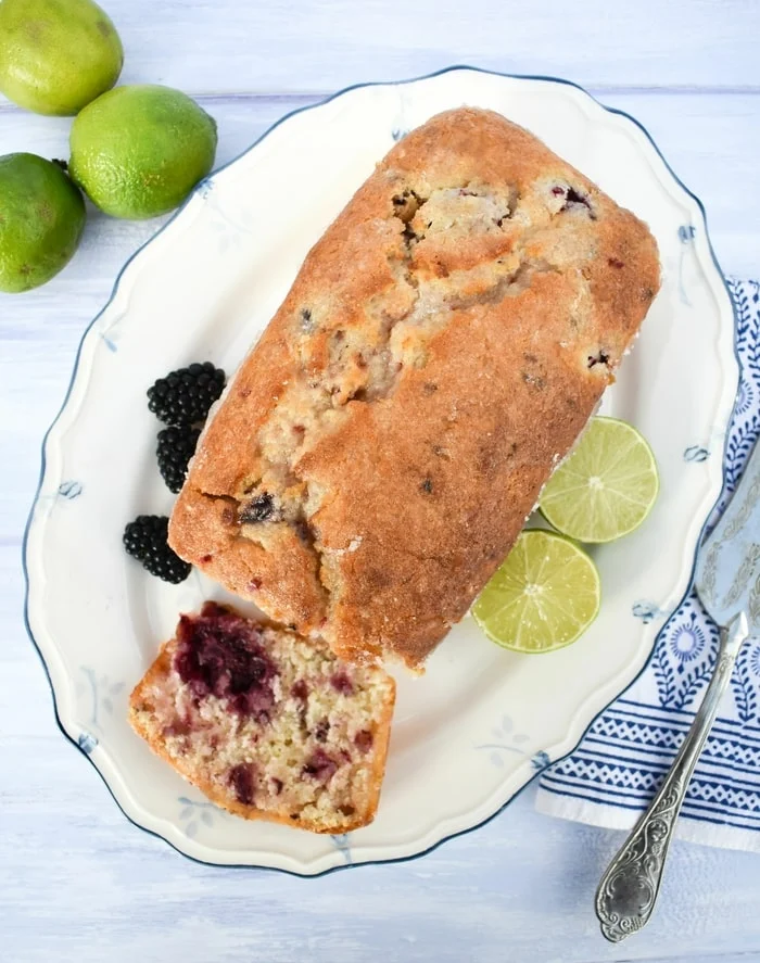 overhead shot of lime blackberry drizzle cake on a platter with blackberries and limes