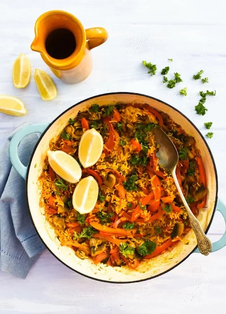 Vegetable Paella in a pan with lemon wedges.